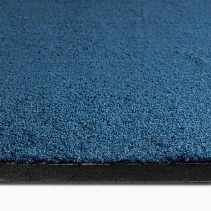 „Eine Nahaufnahme eines strukturierten, blauen Teppichs mit einer schwarzen Bordüre auf weißem Hintergrund.