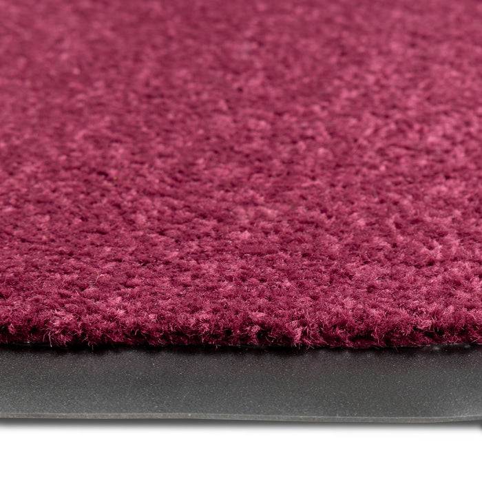 Nahaufnahme eines burgunderfarbenen Teppichs mit strukturierter Oberfläche, die seine Dicke und das Kantendetail vor einem flachen Hintergrund zeigt.