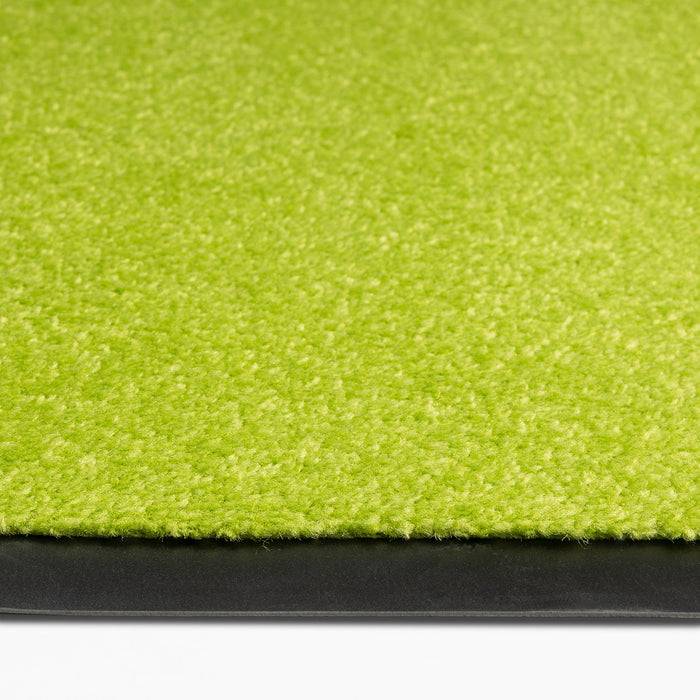 Eine Nahaufnahme eines grünen Teppichs mit einer schwarzen Gummikante, die die Textur und den Materialkontrast zeigt.