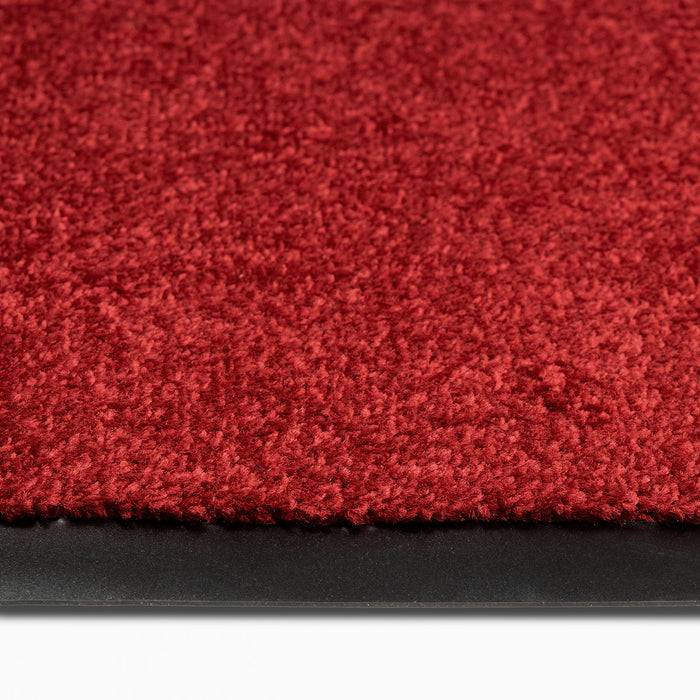 Nahaufnahme eines dunkelroten Teppichs mit gesteppter Textur, begrenzt durch eine dünne schwarze Kante, die einen Kontrast zwischen den Materialien schafft.