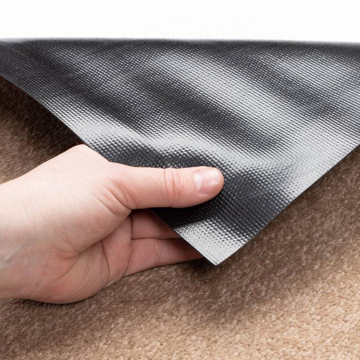 Eine Hand hebt die Ecke einer strukturierten, rutschfesten Matte, die auf einem braunen Teppich liegt, an und zeigt damit ihre Griffigkeit und Materialqualität.