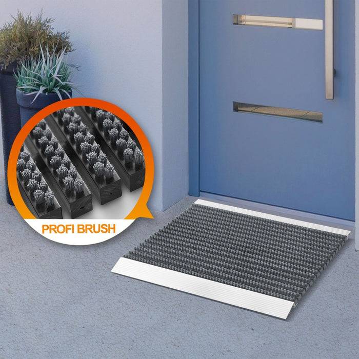Grauer Eingangsläufer vor blauer Tür mit silbernem Griff, ausgestattet mit robusten schwarzen Borsten. Eingesetztes Bild zeigt Nahaufnahme der Borstentextur mit Beschriftung „Profi Brush