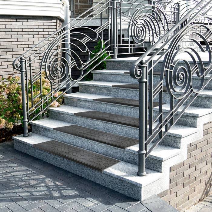 Dekorative Metallgeländer mit Schwungdesign an einer kleinen Außentreppe, umgeben von Ziegelmauern und Gartenpflanzen, die zum Eingang eines Gebäudes führen.