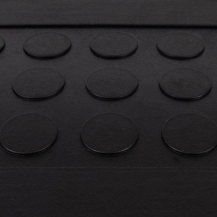 Nahaufnahme einer schwarzen Oberfläche mit einem Raster aus erhabenen kreisförmigen Noppen, möglicherweise ein taktiles Leitsystem, das einen barrierefreien Weg für sehbehinderte Menschen anzeigt.