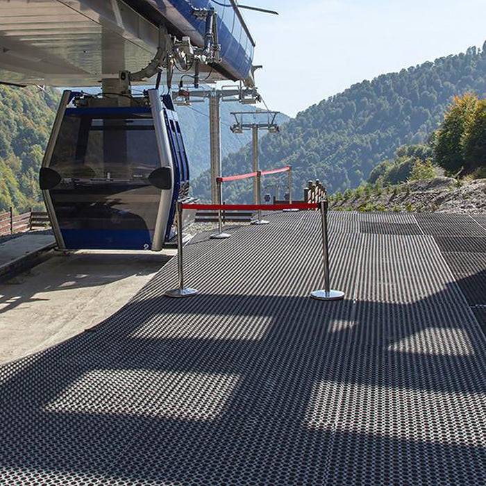 Eine Gondelbahn-Station mit einer blauen Seilbahn, die darüber schwebt. Der Hintergrund zeigt bewaldete Hügel und einen klaren Himmel.