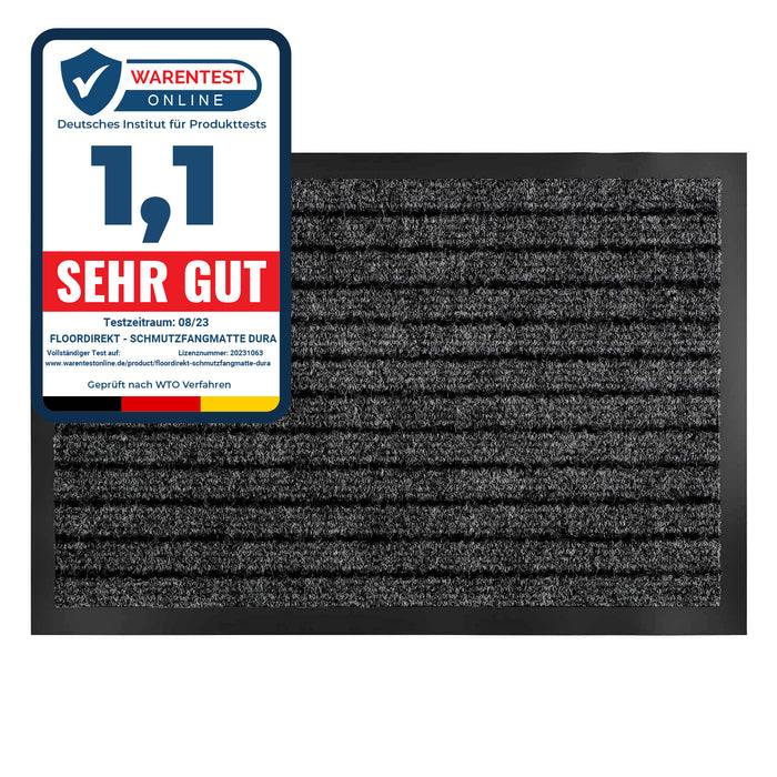 Eine schwarze Fußmatte neben einem Zertifizierungslabel von 'Warentest Online' mit einer Bewertung von '1,1 Sehr Gut', was eine hohe Qualität anzeigt.