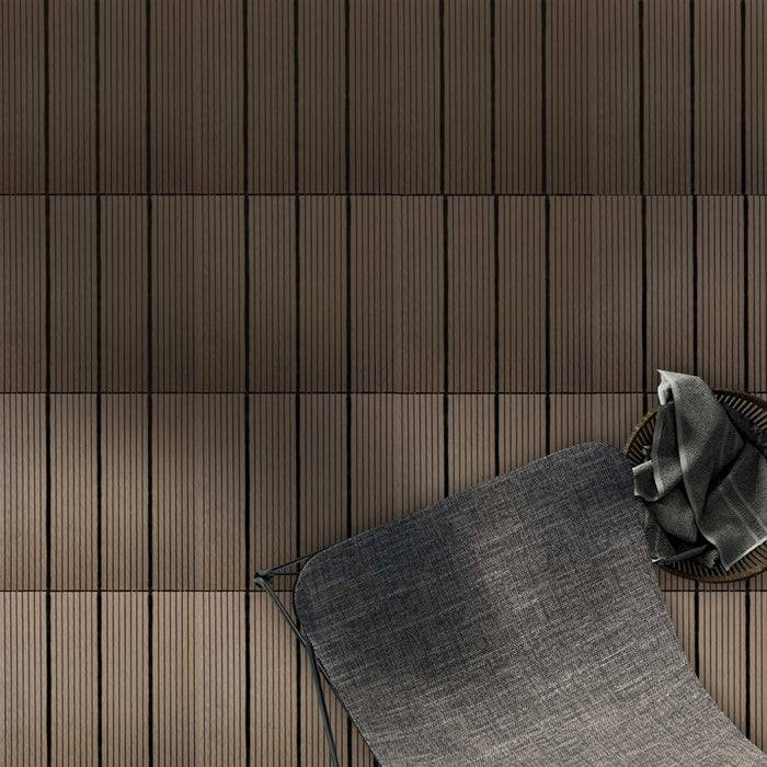 Ein gemütlicher Stuhl mit strukturiertem grauem Kissen und verstreuten Stoffen vor einer vertikal gestreiften Holzwand, das einen minimalistischen Designraum schafft.