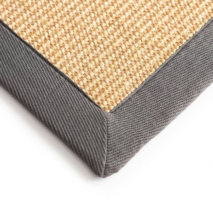 Nahaufnahme einer Ecke einer gewebten beigen Matte mit einem dunkelgrauen Stoffrand.