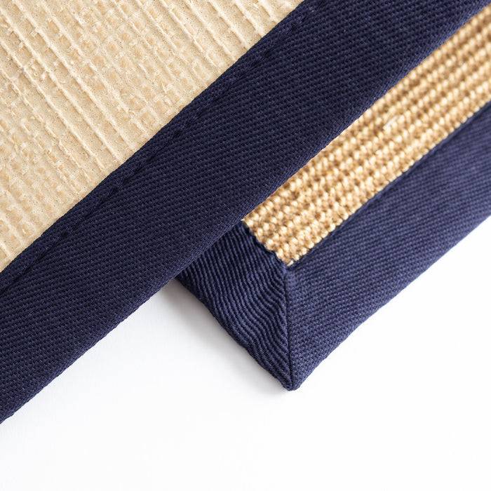 Nahaufnahme von zwei überlappenden Stoffmustern mit unterschiedlichen Texturen: eines ist gerippelt beige, das andere ist gewebt, beide mit marineblauen Kanten versehen.