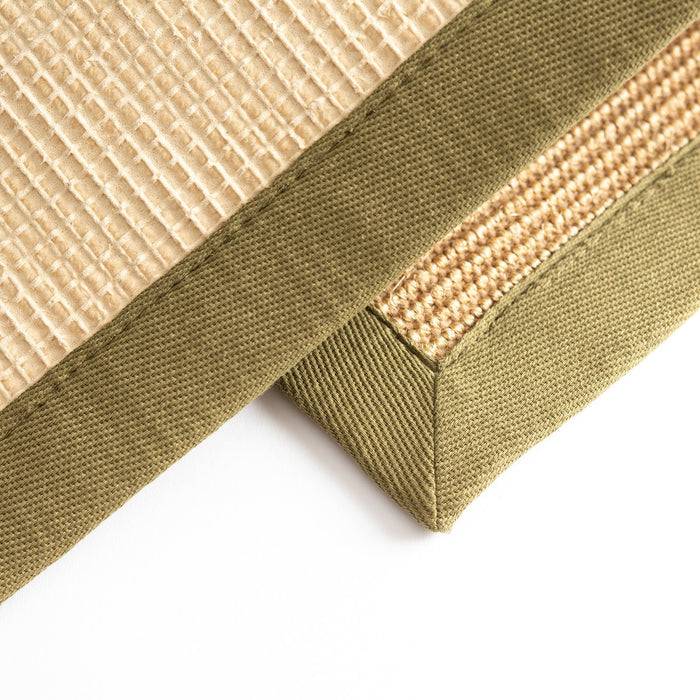 Nahaufnahme einer strukturierten beigefarbenen Matte mit grünem Stoffrand, die gewebte Details und kontrastierende Materialien zeigt.