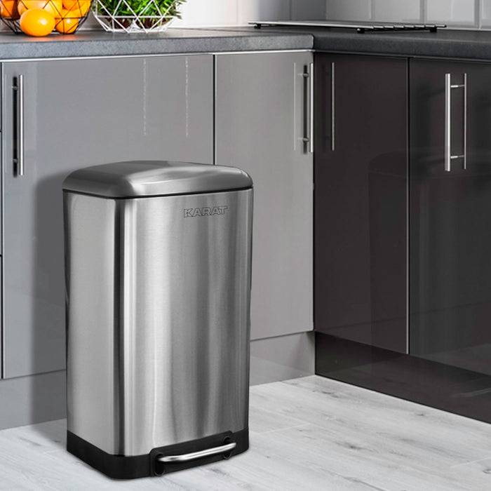 Ein Edelstahl-Mülleimer mit Fußpedal steht in einer modernen Küche mit grauen Schränken und Holzboden.