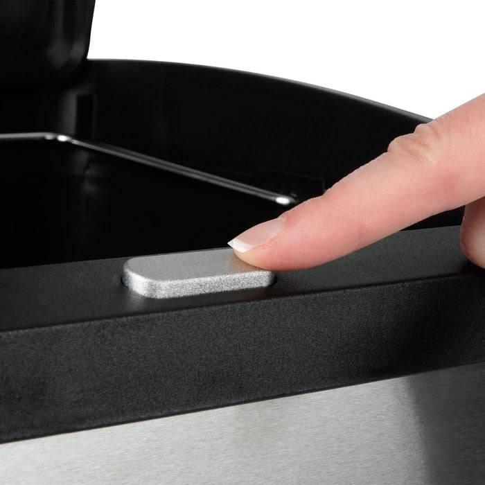 Eine Nahaufnahme eines Fingers einer Person, der die Deckelfreigabetaste an einem Edelstahl-Mülleimer drückt, und zeigt den Berührungsmechanismus.