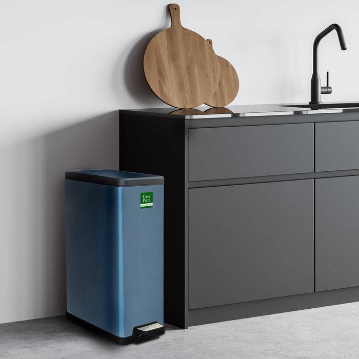 Eine moderne Küchenecke zeigt einen schwarzen Schrank mit einem Waschbecken, ein Holz-Schneidebrett und einen blauen Recycling-Behälter mit der Aufschrift „Nur Kunststoff