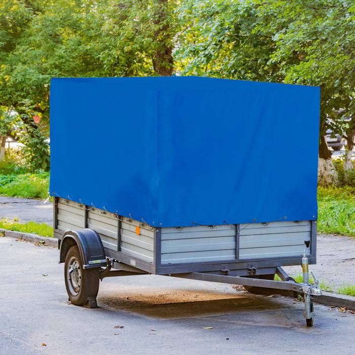Ein kleiner Anhänger, der auf einer Straße geparkt ist, mit einer blauen Plane abgedeckt. Üppige grüne Bäume und Gras befinden sich im Hintergrund.