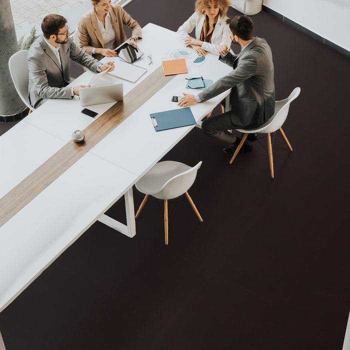 Eine Gruppe von Menschen in Geschäftskleidung sitzt um einen Konferenztisch herum mit Laptops und Dokumenten und diskutiert in einer modernen Büroumgebung.