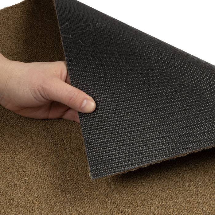 Eine Hand hebt eine Ecke einer schwarzen, gummiartigen Matte an, darunter ist ein strukturierter brauner Teppich sichtbar, der die Dicke und Textur des Materials zeigt.