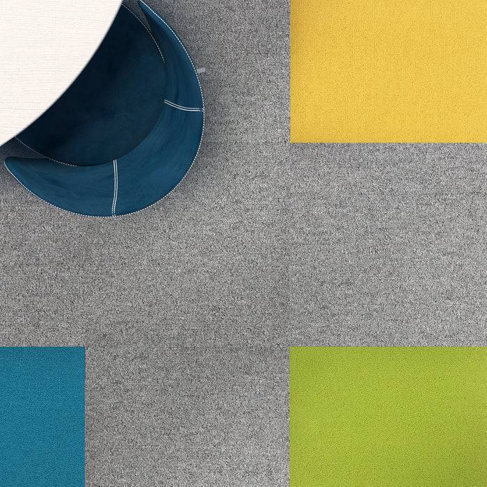 Luftaufnahme eines runden weißen Tisches mit einem blauen Stuhl auf einem karierten Boden, bestehend aus Abschnitten von grauem, gelbem, blauem und grünem Teppich.