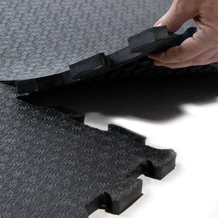 Eine Hand legt eine verschlungene schwarze Bodenmatte auf eine Oberfläche und zeigt deren einfache Montage und strukturiertes Muster für Griffigkeit.