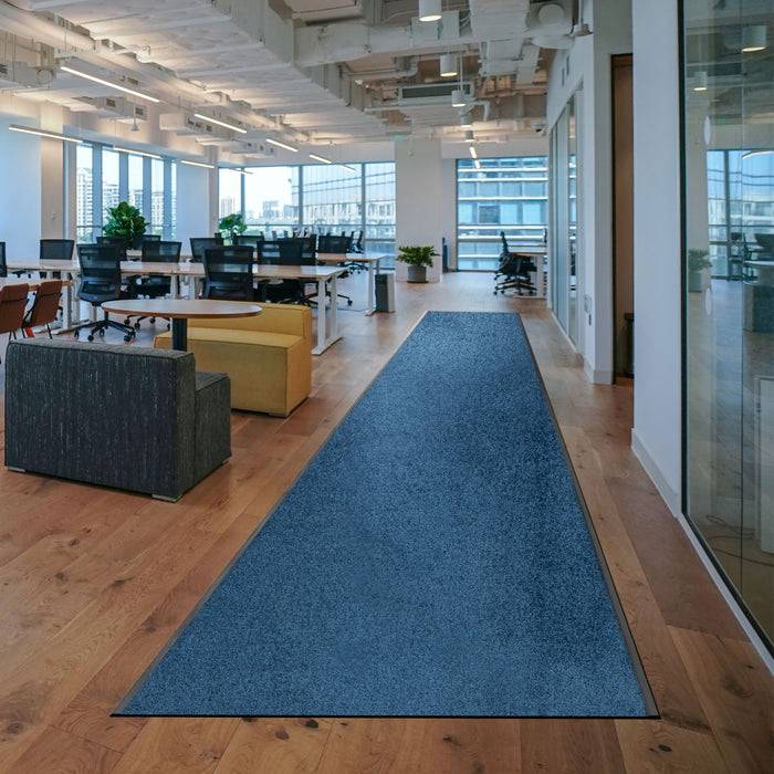 Ein offenes Bürokonzept mit großen Fenstern, moderner Möblierung und einem langen blauen Teppich, der sich durch den Raum erstreckt.