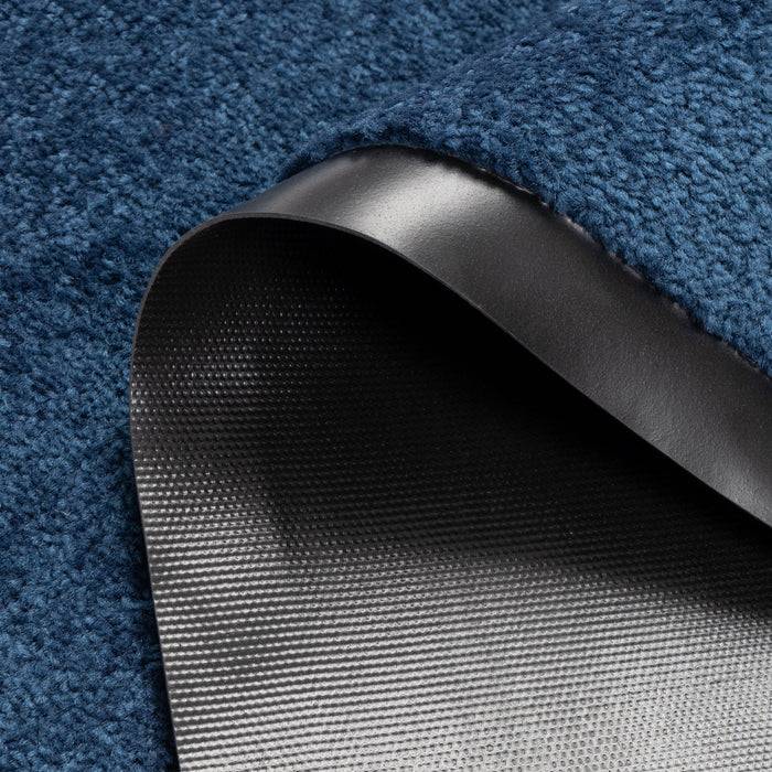 Eine Nahaufnahme eines blauen Teppichs mit einer umgeschlagenen Ecke, die ein schwarzes Gummiunterlage offenbart und seine Textur und Material zeigt.
