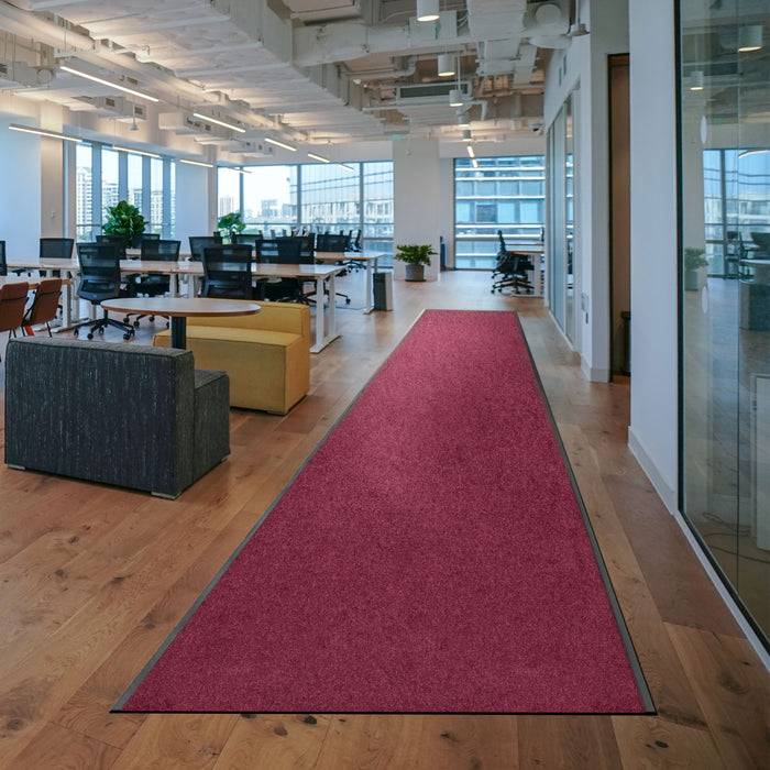 Moderner Büroraum mit großen Fenstern, Holzfußboden und einem roten Läuferteppich, der zu einem Sitzbereich mit Pflanzen und Schreibtischen führt.