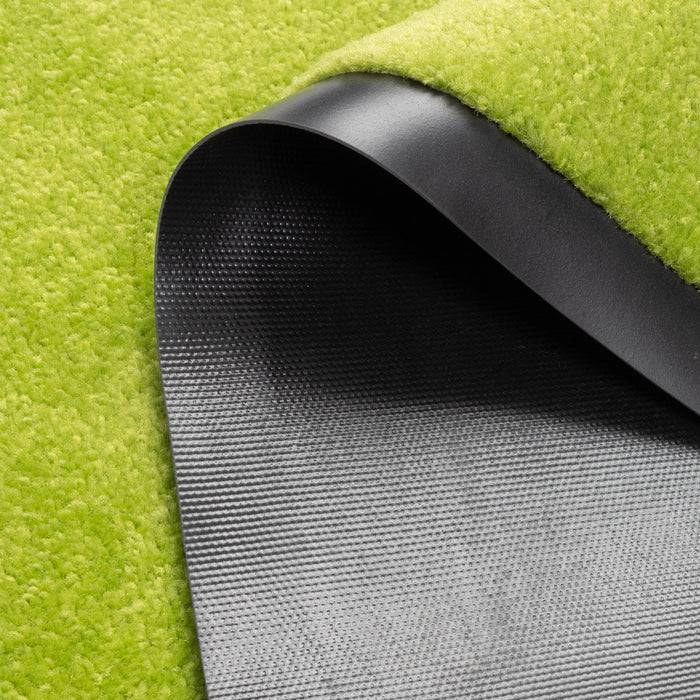 Eine Nahaufnahme eines grünen, strukturierten Teppichs mit einer Gummirückseite, die an einer Ecke aufgerollt ist und das dunkle, rutschfeste Material darunter zeigt.