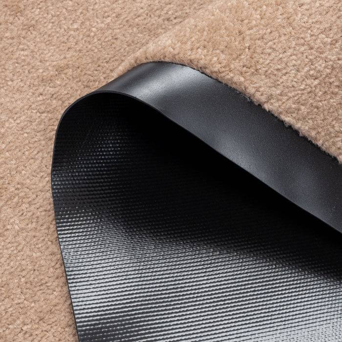 Ein gefalteter Bereich eines beigen Teppichs zeigt eine schwarze Gummi-Antirutschmatte darunter.