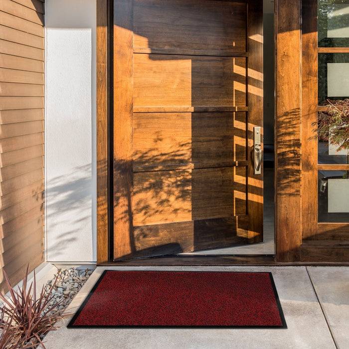 Eine moderne Holz-Eingangstür mit vertikalen Paneelen steht leicht offen und wirft Schatten. Ein roter Türvorleger liegt davor auf einem sauberen Eingangsweg.