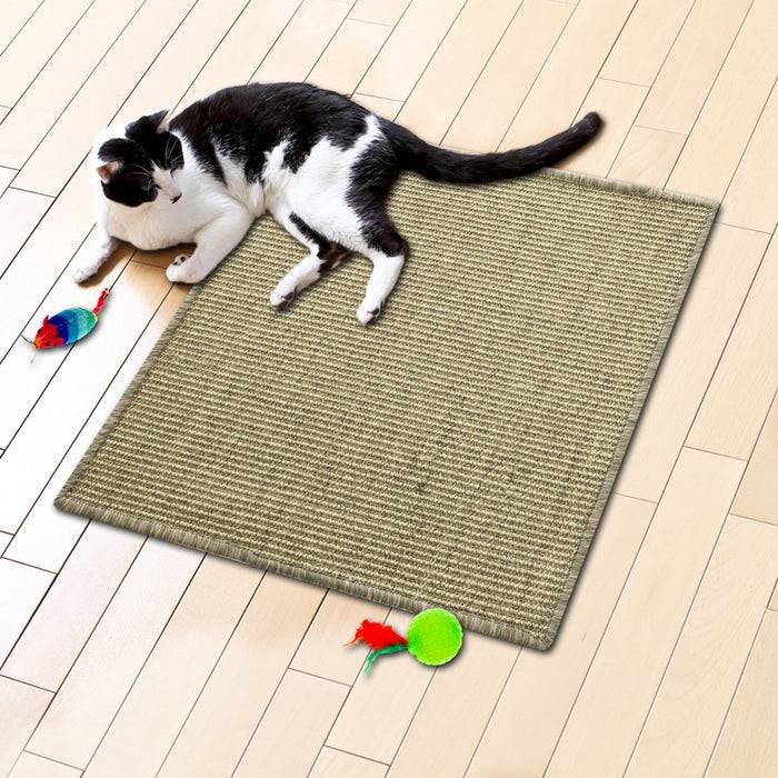 Eine schwarzweiße Katze liegt auf einem geflochtenen Teppich auf einem Holzboden, umgeben von bunten Spielzeugmäusen.