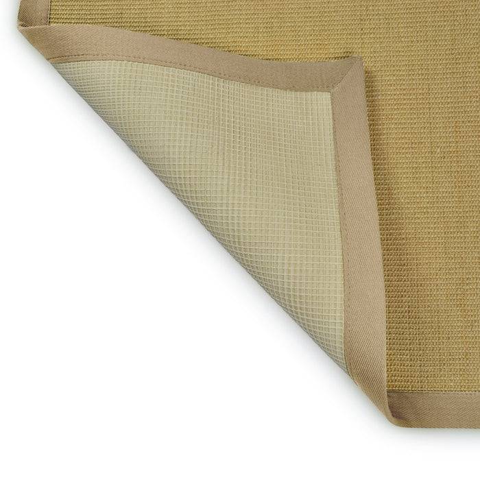 Eine Ecke eines beigen Stoffteppichs ist zurückgeklappt und zeigt ein rutschfestes Gittermuster auf der Unterseite. Der Teppich liegt auf weißem Untergrund.