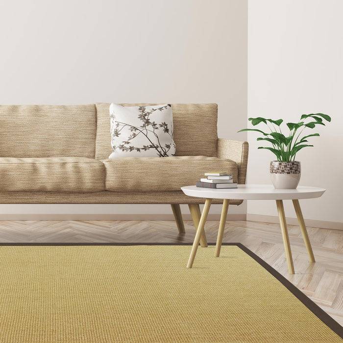 Ein minimalistisches Wohnzimmer mit einem beigen Sofa, einem Blumenkissen, einem kleinen weißen Tisch, einer Topfpflanze und einem grünen Teppich auf einem Holzboden.