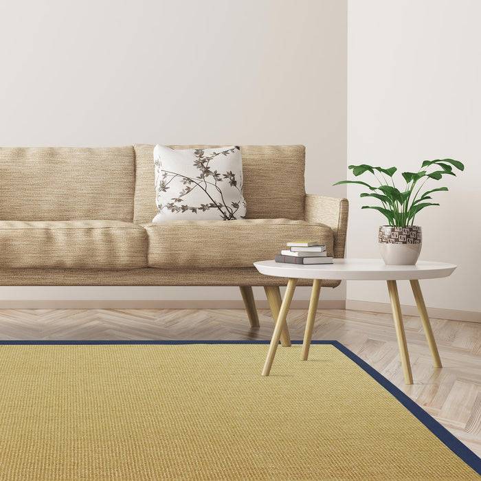 Ein gemütliches Wohnzimmer mit einem beigen Sofa, einem Blumenkissen, einer Topfpflanze auf einem weißen Couchtisch und einem gelben Teppich mit blauem Rand.