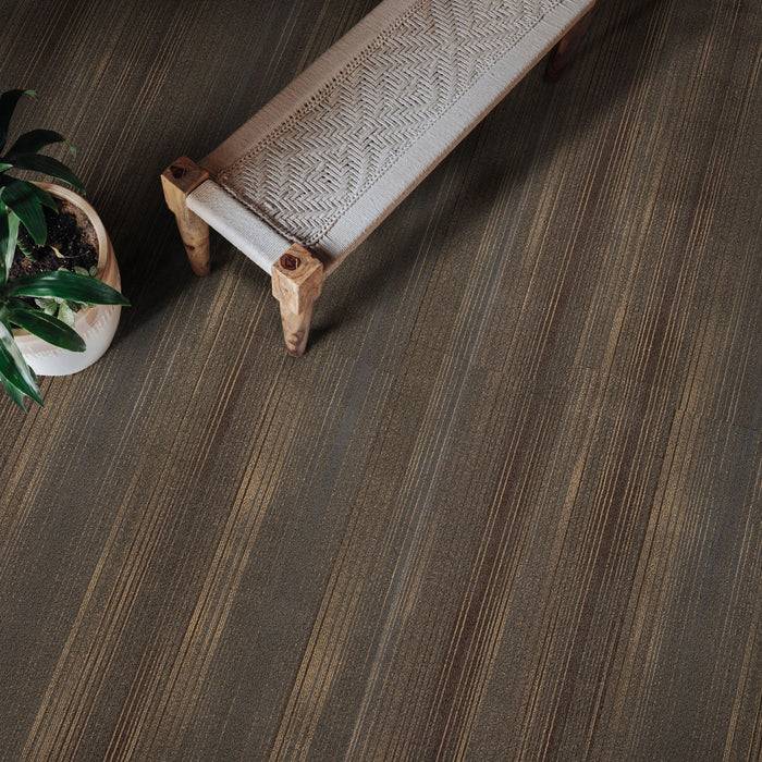 Eine leichte Holzbank mit gewebtem Muster steht auf einem strukturierten, gestreiften Boden neben einer grünen Topfpflanze und schafft eine ruhige Atmosphäre.