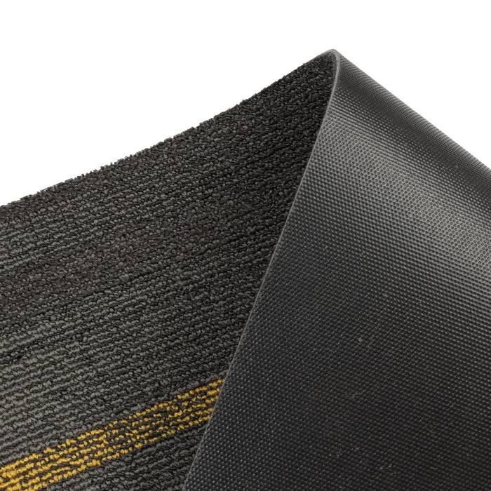Das Bild zeigt eine strukturierte schwarze Matte mit einem erhabenen gelben Streifen, der teilweise aufgerollt ist und seine glatte Unterseite enthüllt.