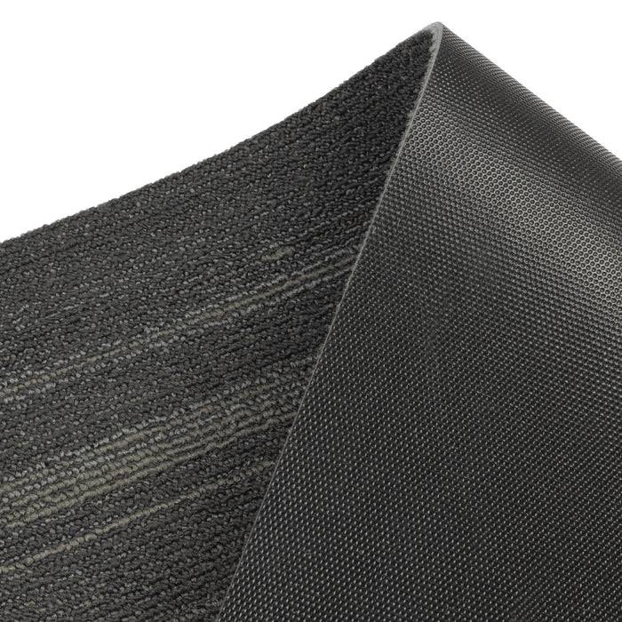 Nahaufnahme der strukturierten Oberfläche einer grauen Gummimatte, die ein subtiles Streifenmuster und eine geschwungene Kante auf einfachem Hintergrund zeigt.