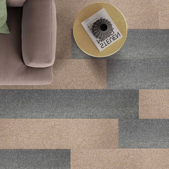 Draufsicht auf ein beiges Sofa neben einem goldfarbenen runden Tisch mit einer Zeitschrift und einer schwarzen Tasse darauf, platziert auf einem Teppich mit geometrischem Muster.