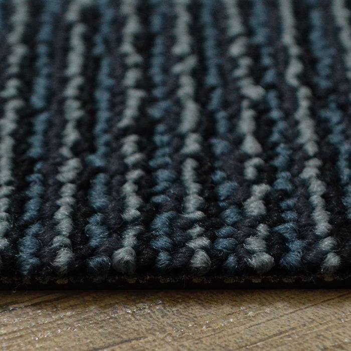 „Eine Nahaufnahme eines strukturierten, gestreiften Teppichs mit einer Mischung aus dunklen und hellen Blautönen, auf einem Holzboden verlegt.