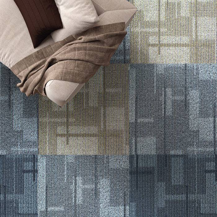 Ein Patchwork-Teppich in Blau- und Beigetönen mit einem modernen geometrischen Muster liegt auf dem Boden unter einem beigen Stoffsofa.