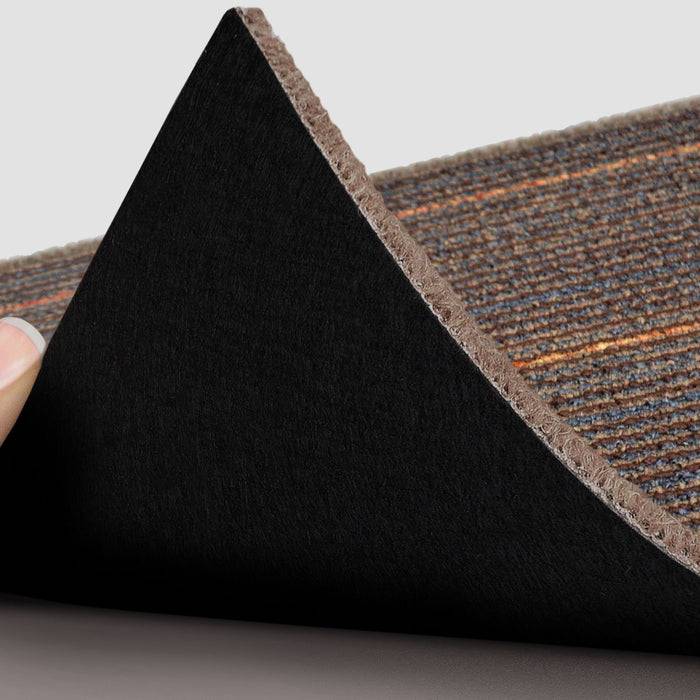 Eine Hand hebt die Ecke eines braunen gestreiften Teppichs, um dessen schwarze rutschfeste Rückseite zu enthüllen.