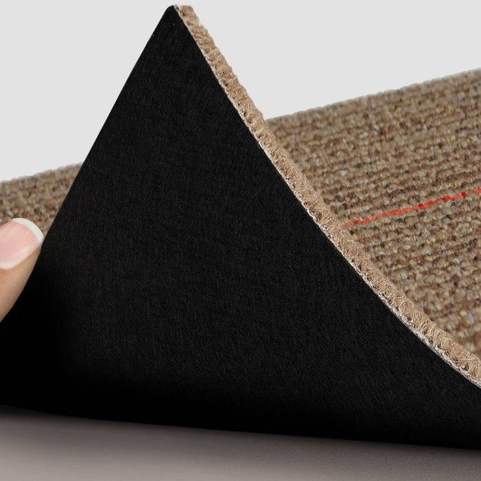 Die Hand einer Person hebt die Kante eines braunen Teppichs an und offenbart die Unterseite mit einem feinen roten Fadenelement.