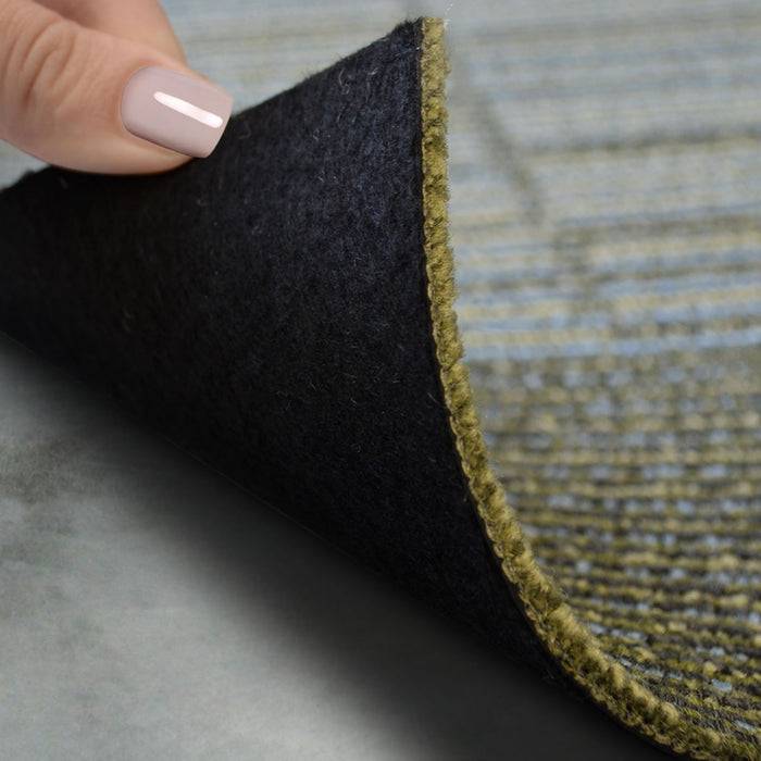 Die Hand einer Person hebt eine Ecke eines gestreiften Teppichs, um seine Rückseite zu zeigen, wobei die Unterseite Textur und Materialkontrast offenbart.