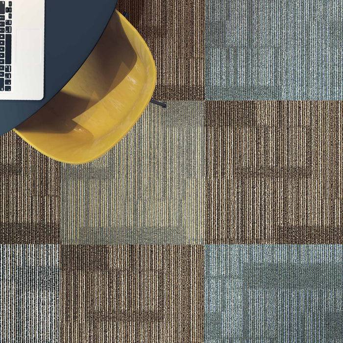 Luftaufnahme eines Laptops auf einem runden Schreibtisch neben einem gelben Stuhl, platziert auf einem karierten Teppich mit Braun- und Blautönen.