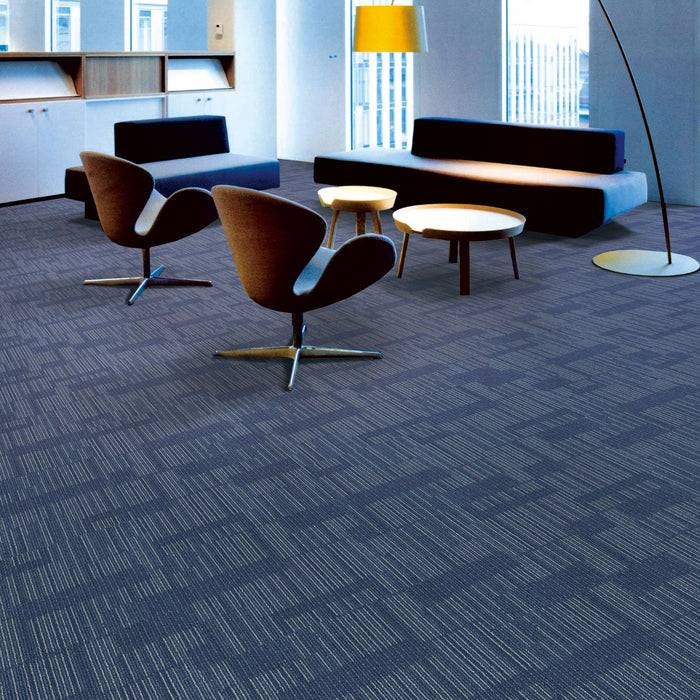 Eine moderne Bürolounge mit drei Stühlen, einem Sofa und zwei runden Tischen. Ein Teppich mit geometrischem Muster bedeckt den Boden. Natürliches Licht erfüllt den Raum.