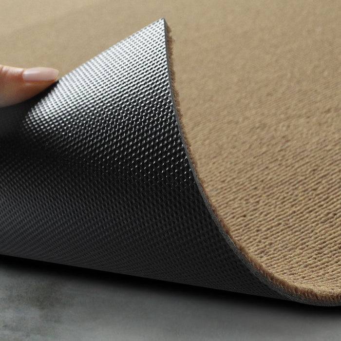 Eine Hand hebt die Ecke eines strukturierten, zweischichtigen Teppichs und zeigt eine weiche beige Oberfläche und eine schwarze rutschfeste Rückseite, wodurch dessen Hafteigenschaft veranschaulicht wird.
