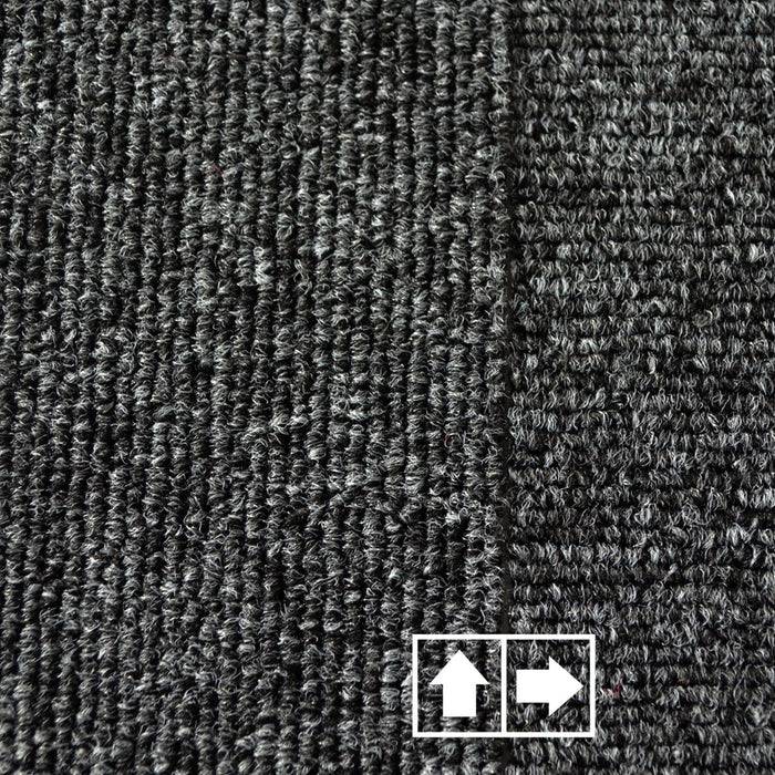 Eine Nahaufnahme eines strukturierten grauen Teppichs mit einer sichtbaren weißen Nahtlinie. Zwei Pfeile in einem Kästchen zeigen nach oben und rechts.