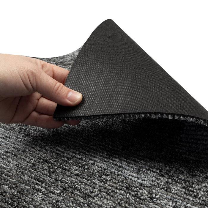 Eine Hand hebt eine Ecke eines wendbaren grauen Teppichs an und zeigt die schwarze rutschfeste Unterseite.