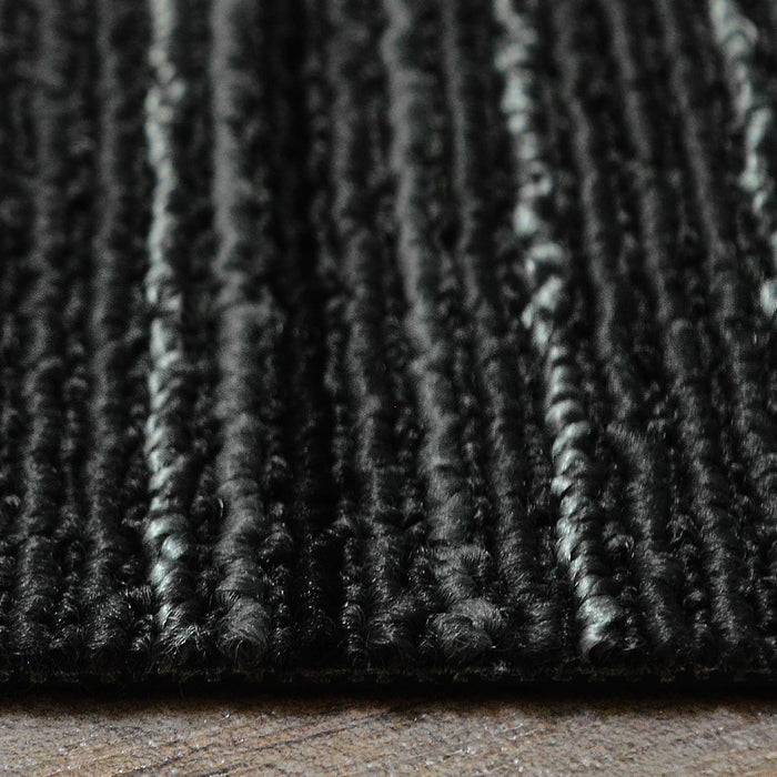 Eine Nahaufnahme eines strukturierten schwarz-grau gestreiften Teppichs auf einem Holzboden, die das lineare Muster des Teppichs und sein weiches Material hervorhebt.