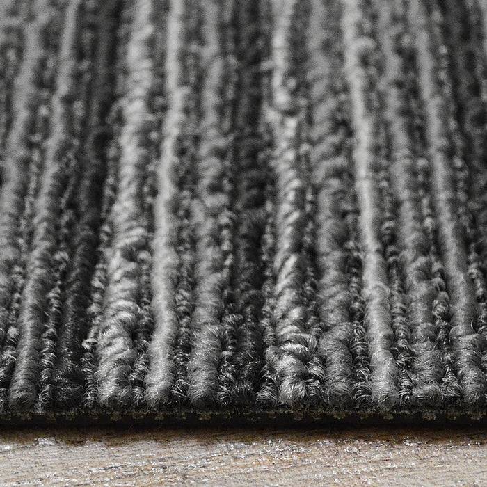 Ein strukturierter grauer Teppich mit vertikalen Linien, in einer Nahaufnahme gezeigt, der auf einem Holzboden liegt.