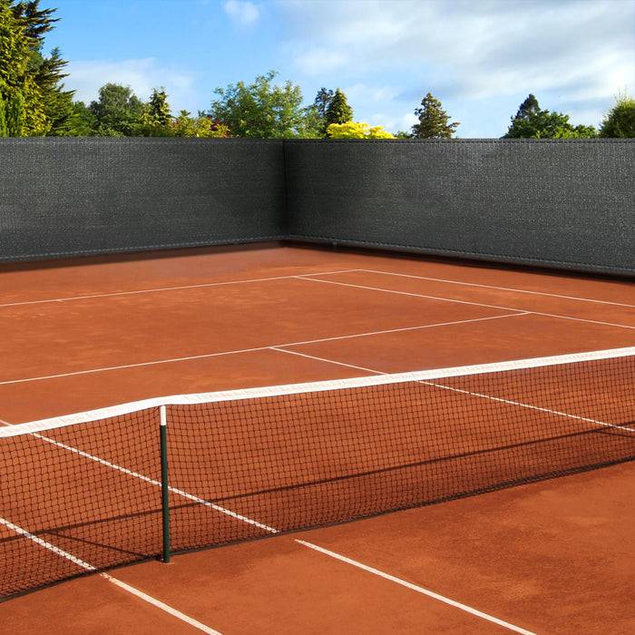 Ein Tennisplatz aus rotem Lehm mit einem Netz in der Mitte, umgeben von grünen Bäumen und einem bewölkten Himmel.
