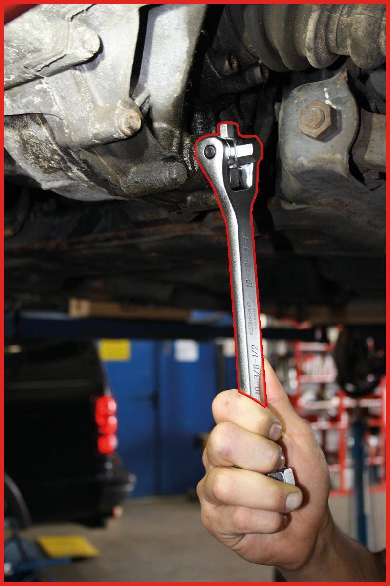 Eine Hand benutzt einen Schraubenschlüssel, um ein Bauteil unter einem Fahrzeug einzustellen, was auf eine Autoreparatur- oder Wartungsaktivität hinweist.